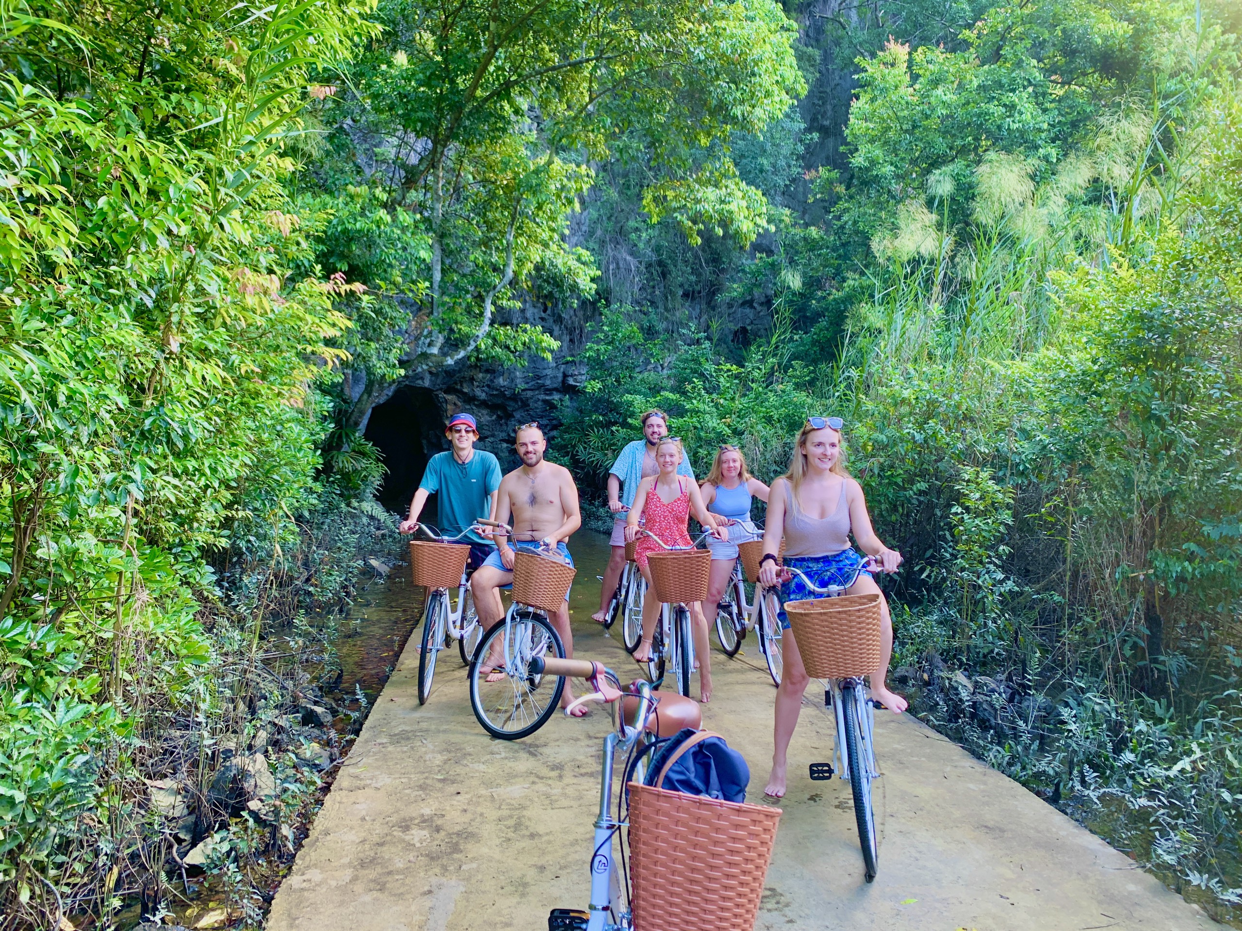Group of cyclists riding a shaded road through dense jungle in Cat Ba National Park
