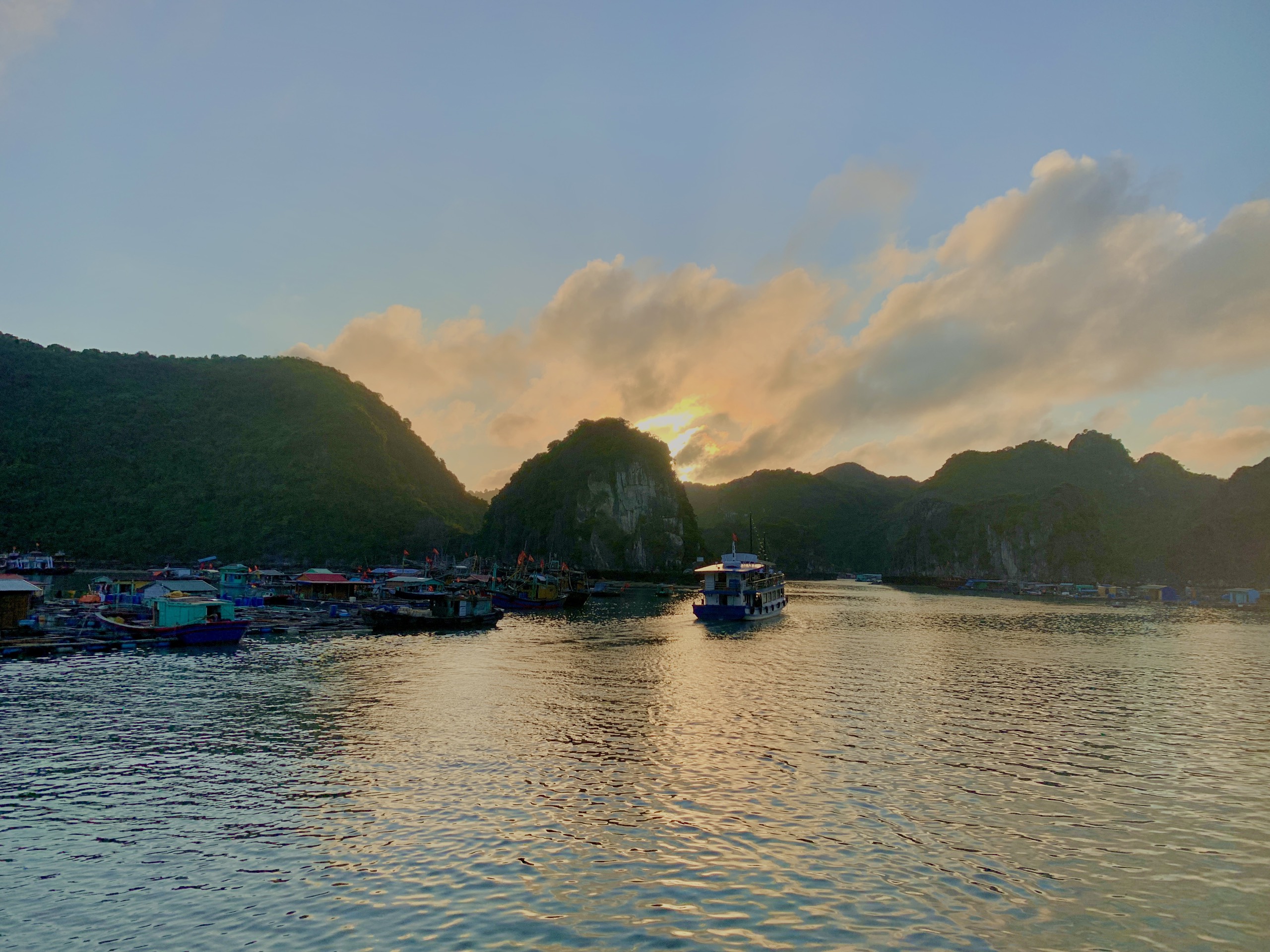 Golden sunset over Lan Ha Bay with wooden boats moored between limestone karsts, Cat Ba Island