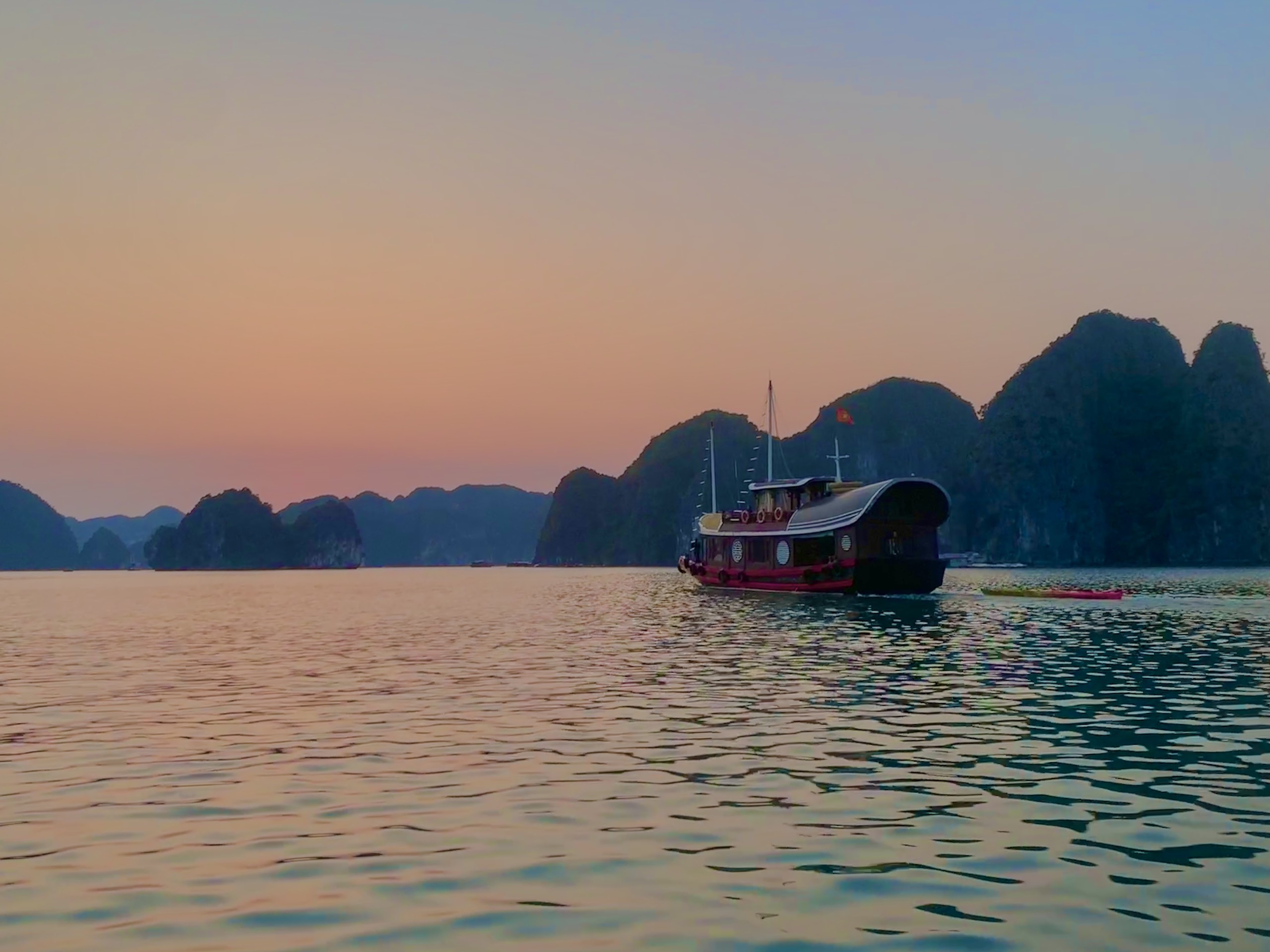 Traditional wooden junk boat anchored in calm water at sunset in Lan Ha Bay