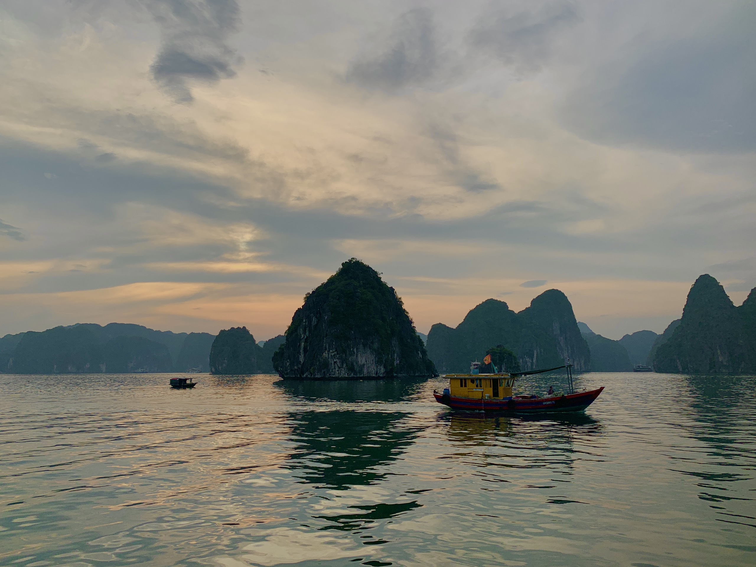 Wooden boat on calm water at sunset between limestone karsts, Lan Ha Bay