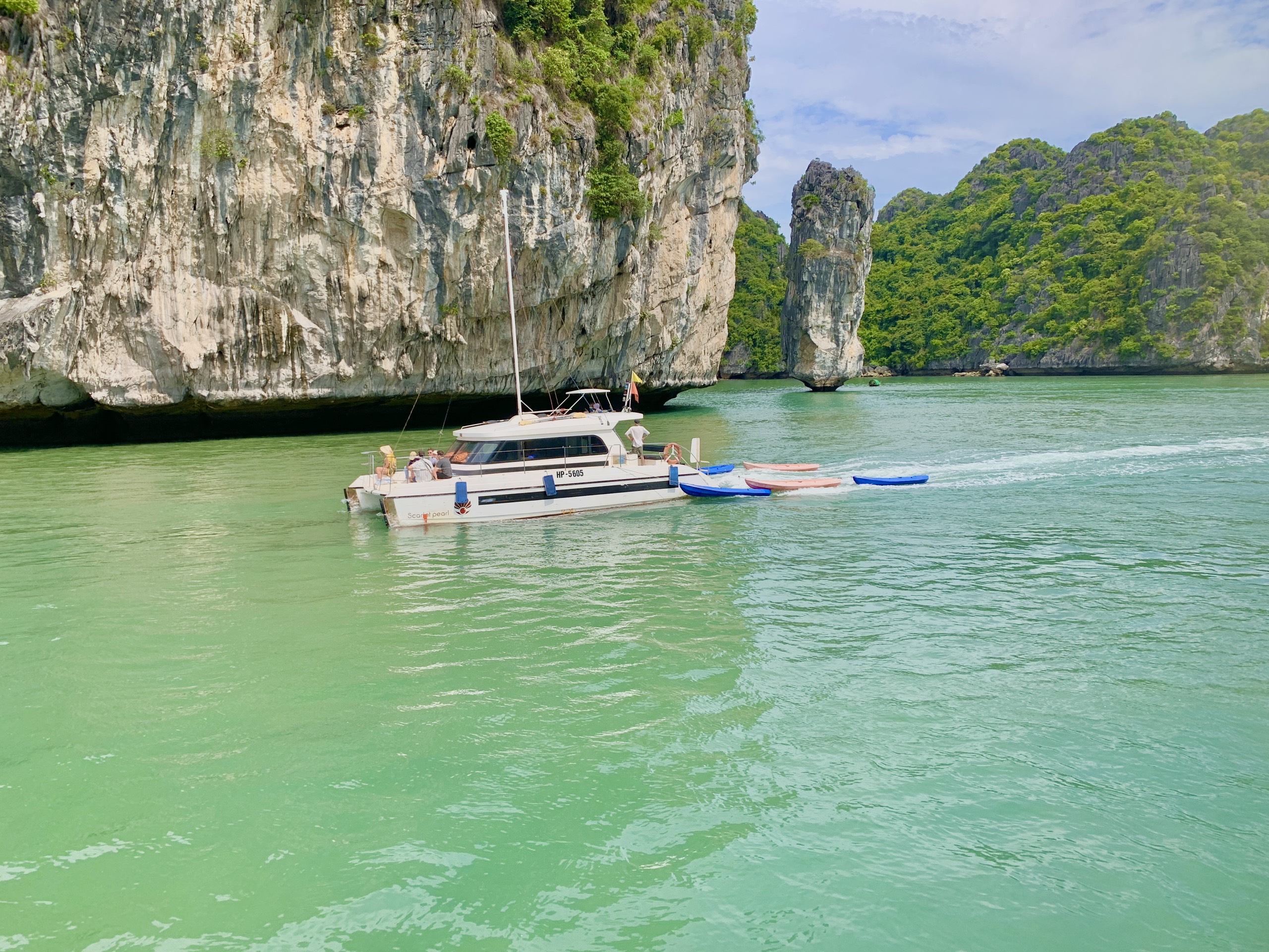Small passenger boat crossing calm turquoise water between limestone islands, Cat Ba