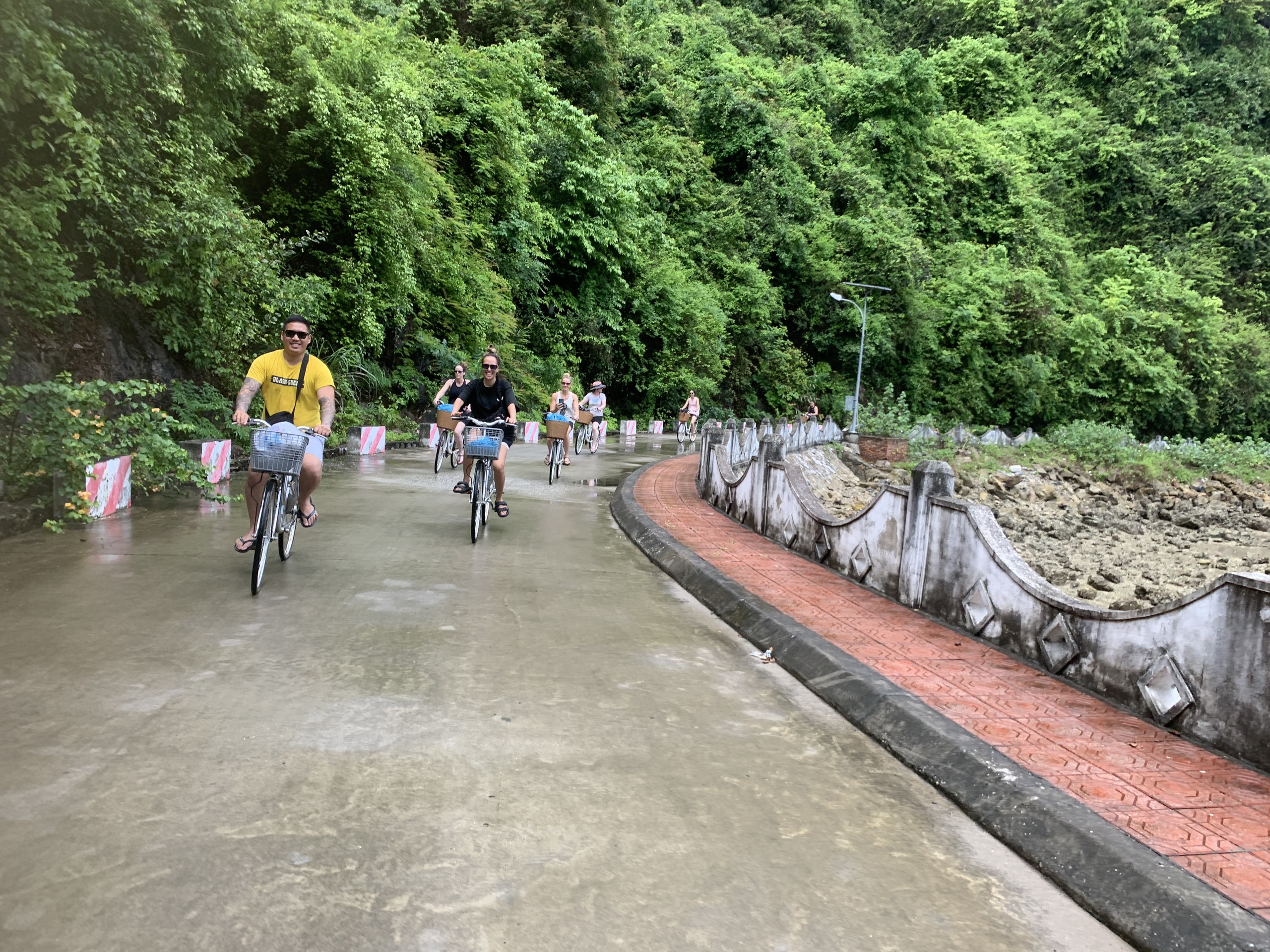 Cyclists riding along an empty paved road beside limestone cliffs in Viet Hai village, Cat Ba