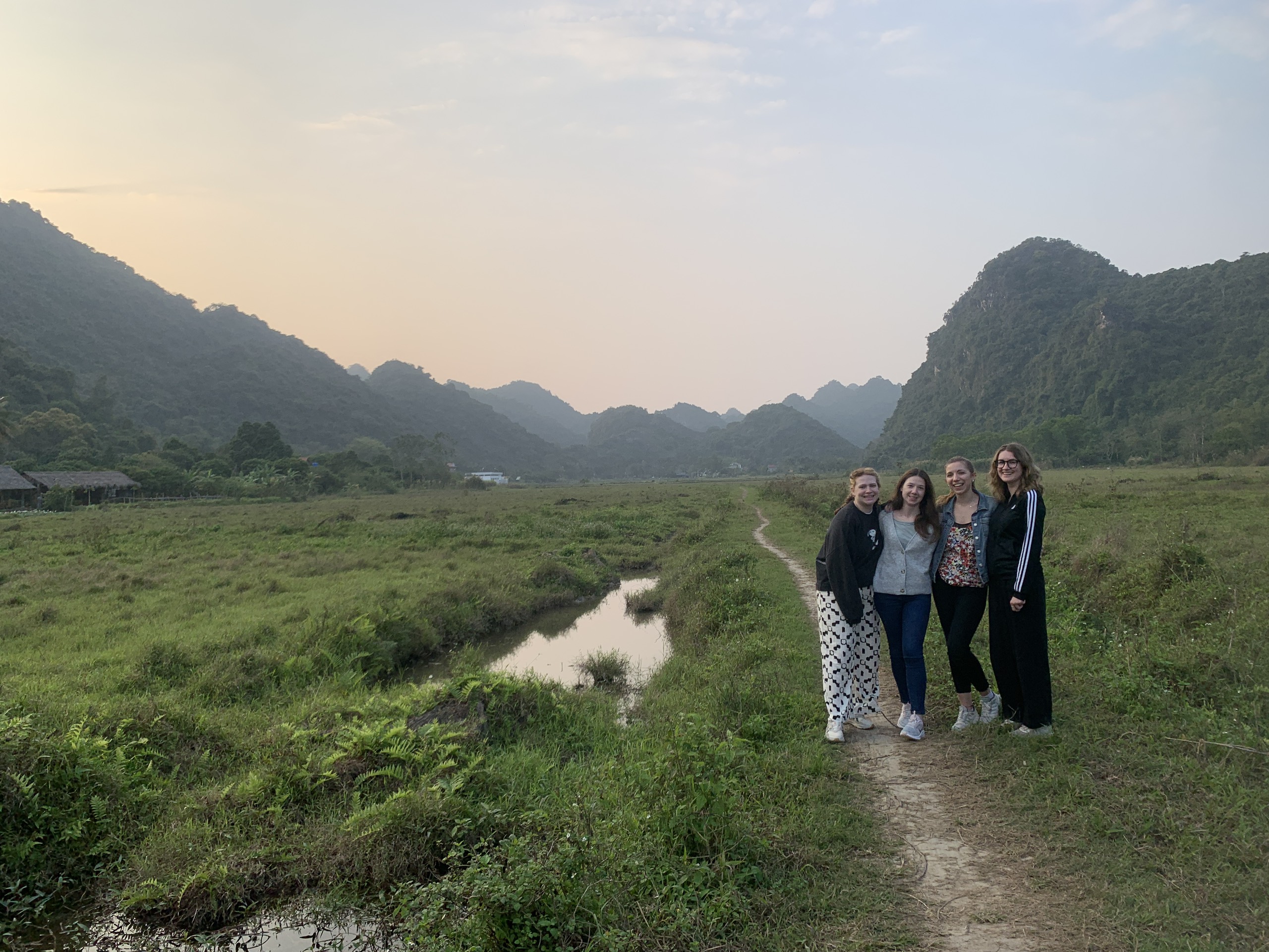 Travellers walking a path through misty fields below limestone mountains in Viet Hai valley, Cat Ba