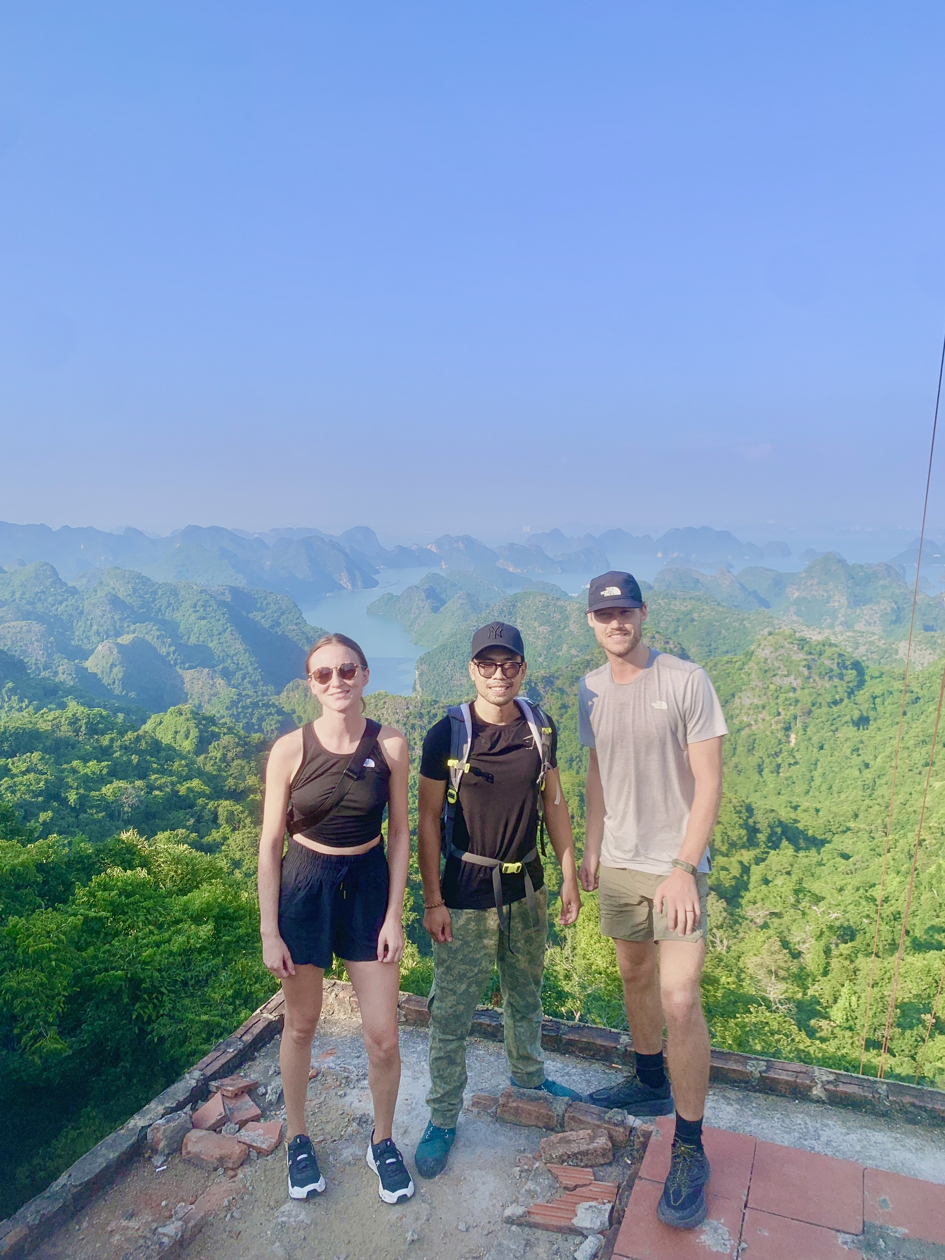 Three travellers standing at a viewpoint overlooking limestone islands and sea, Cat Ba