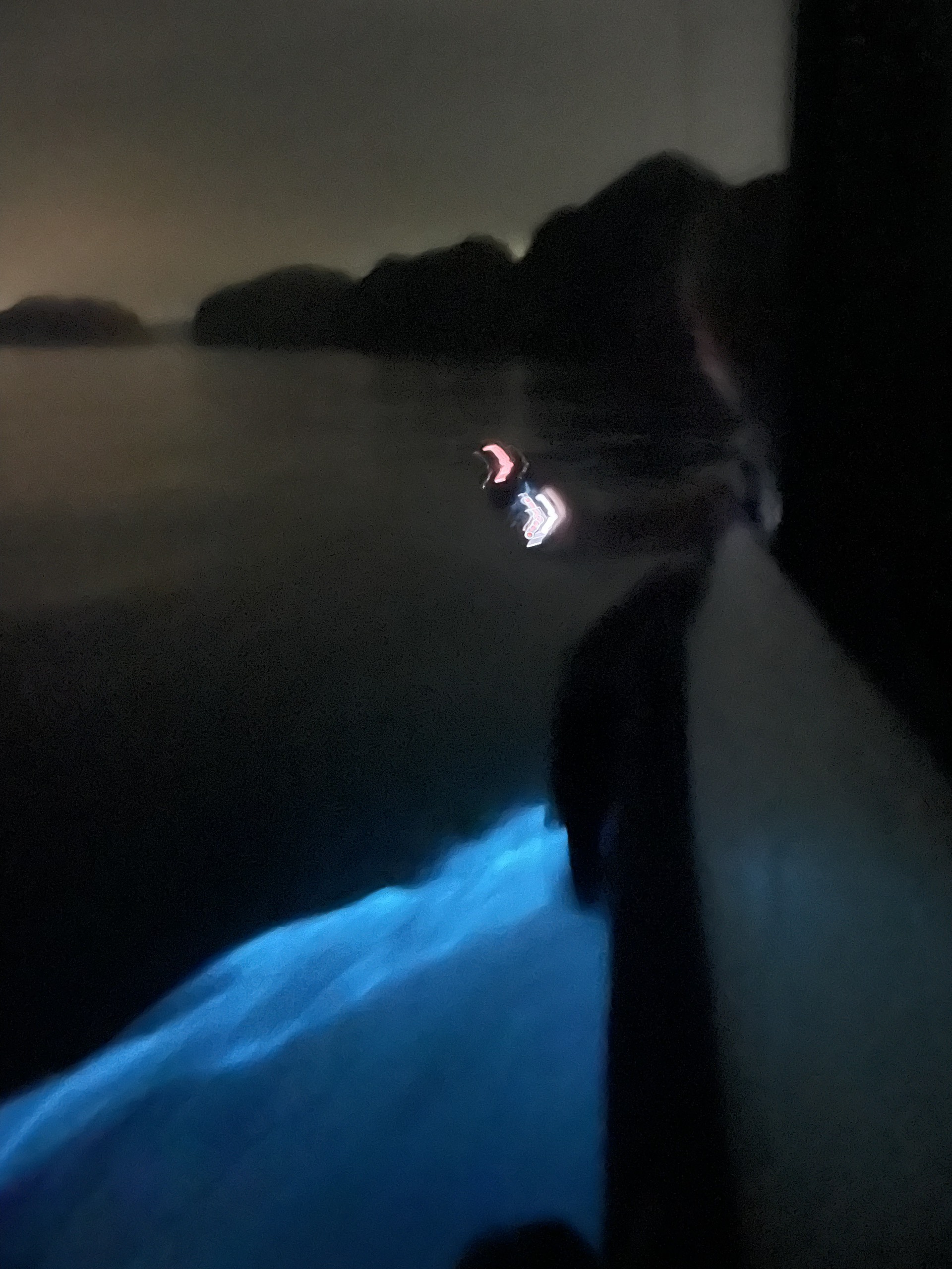 Kayaker with a headlamp on dark water at night in Lan Ha Bay