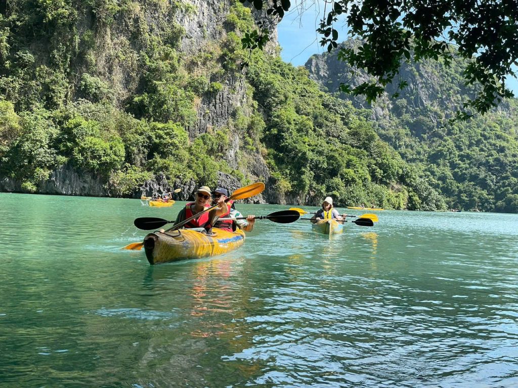 Guests kayaking through crystal clear emerald waters of Lan Ha Bay surrounded by limestone karst formations, Cat Ba Island