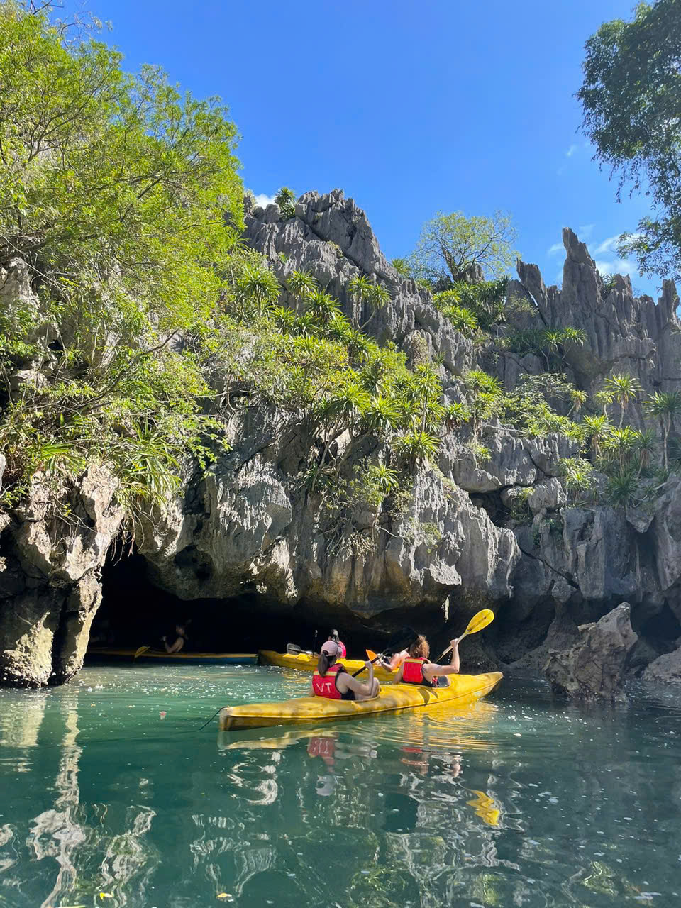 Kayakers paddling through a limestone sea cave into a hidden lagoon in Lan Ha Bay, Vietnam