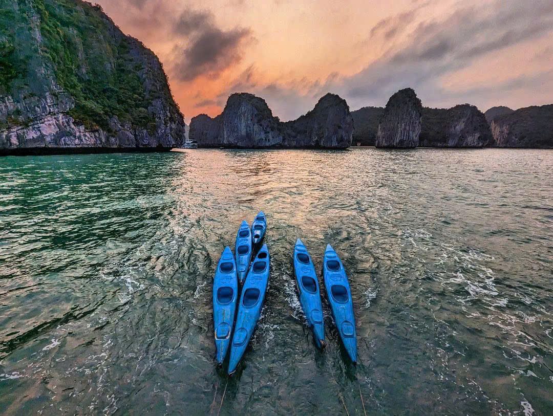 Blue kayaks lined up on the beach at sunset in Lan Ha Bay