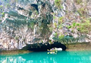 Small boat entering a limestone cave arch in Lan Ha Bay