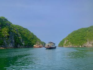 Boat passing between green limestone karsts in Lan Ha Bay