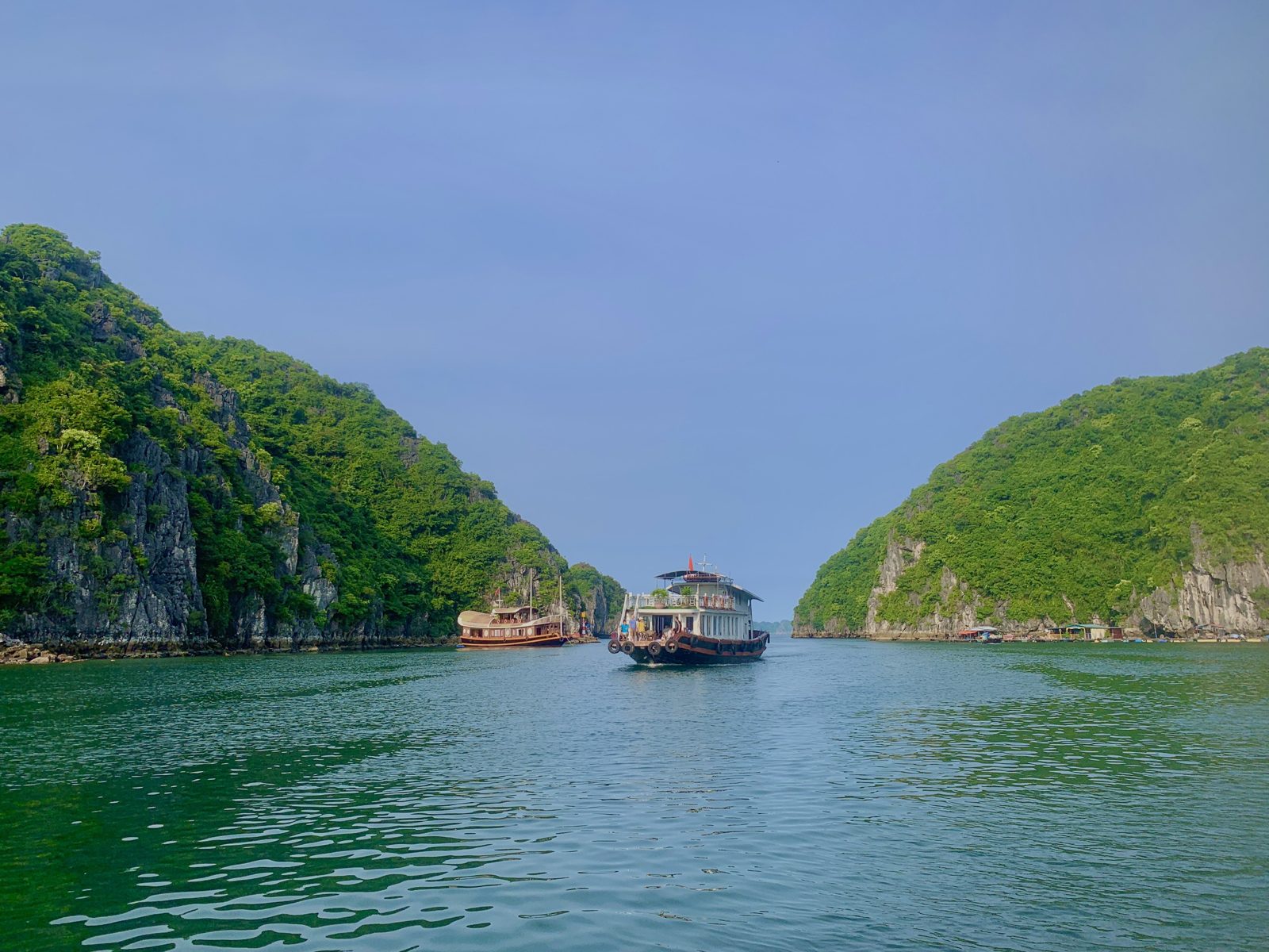 Boat passing between green limestone karsts in Lan Ha Bay
