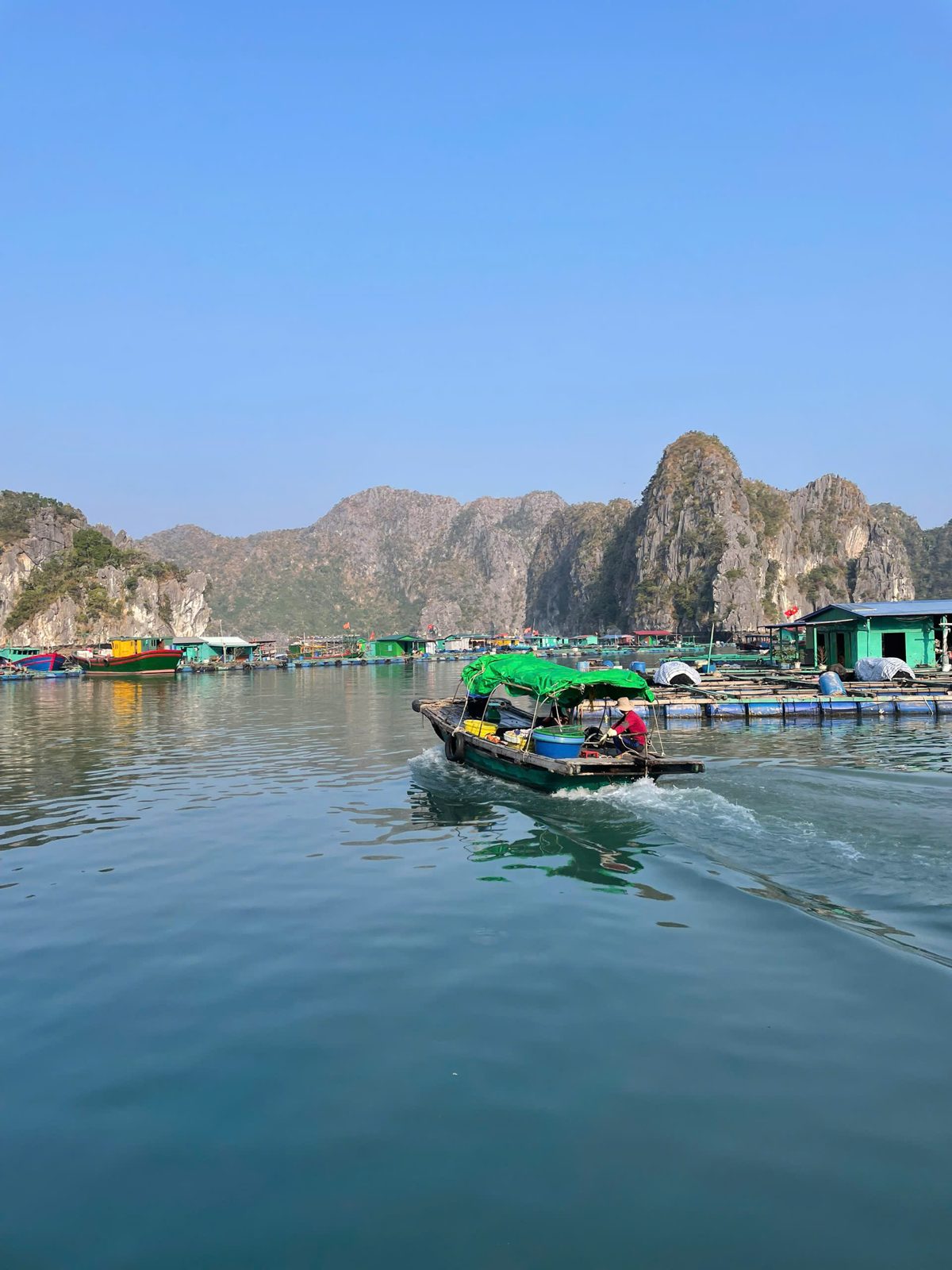 Small boat passing a floating fish farm in Lan Ha Bay, Cat Ba Island