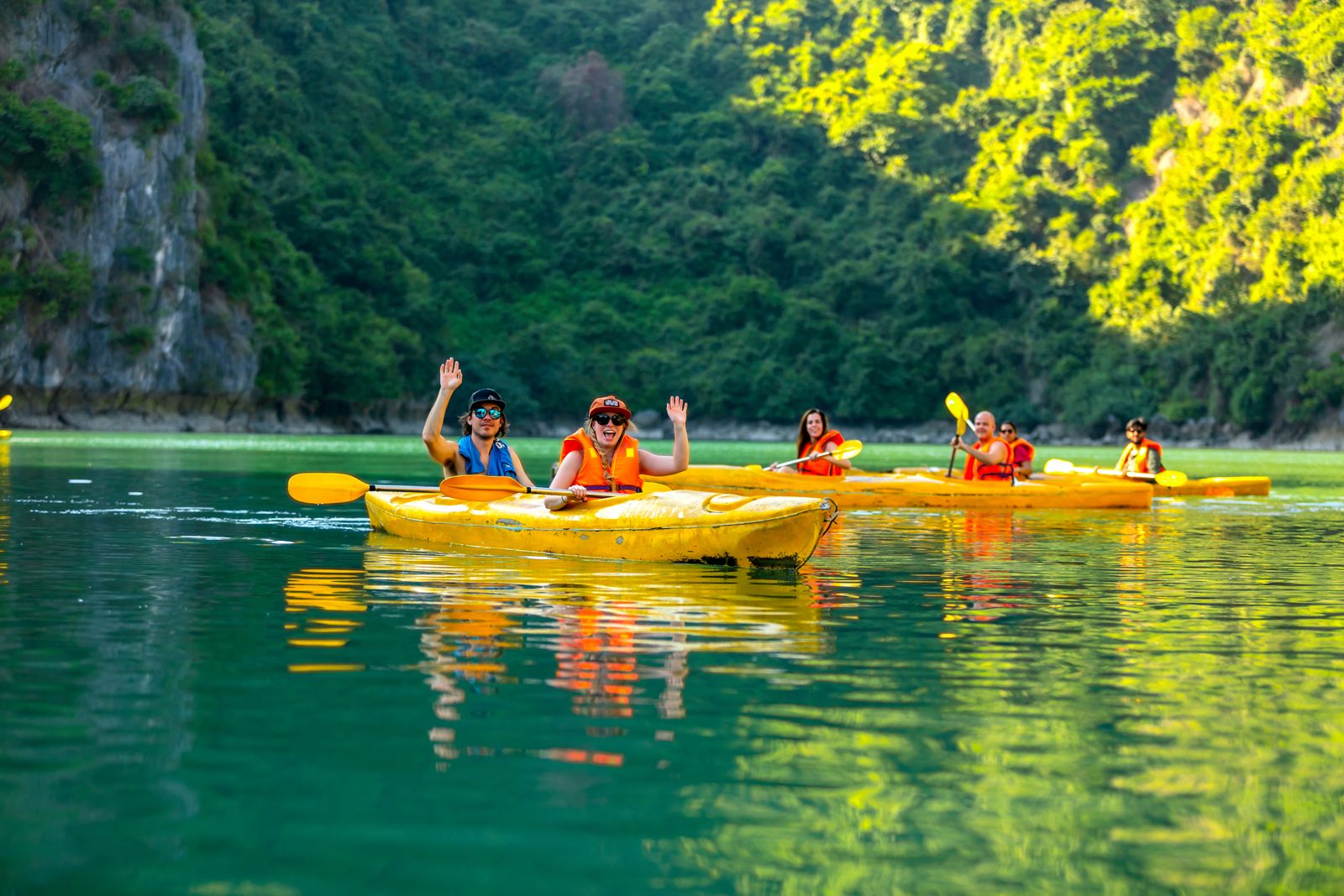 Group of kayakers on emerald green water below jungle-covered karsts, Lan Ha Bay
