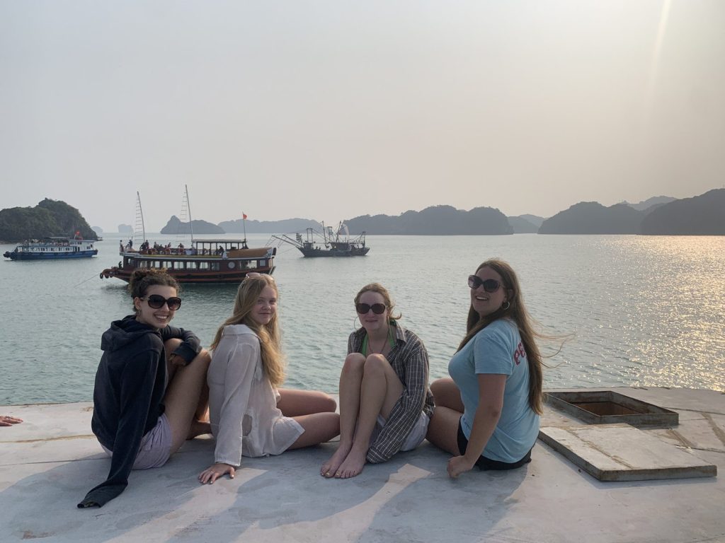 Group of travellers sitting on a pier looking over Lan Ha Bay