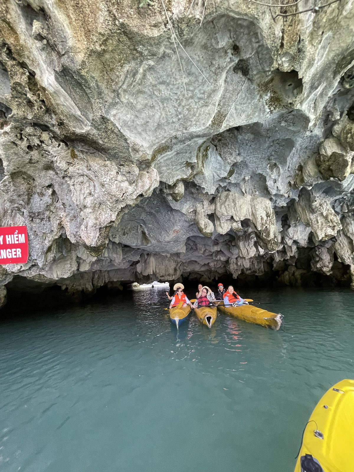 Yellow kayak entering a limestone cave passage in Lan Ha Bay, Cat Ba Island