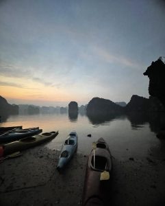 Kayaks on the shore at dawn with mist over Lan Ha Bay