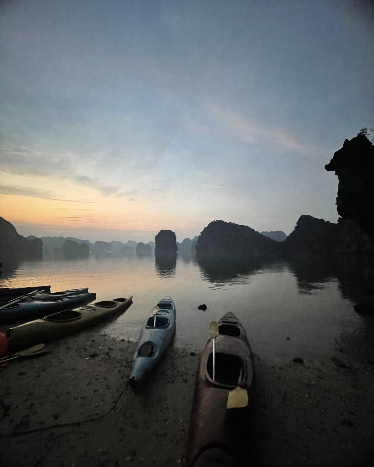 Kayaks on the shore at dawn with mist over Lan Ha Bay