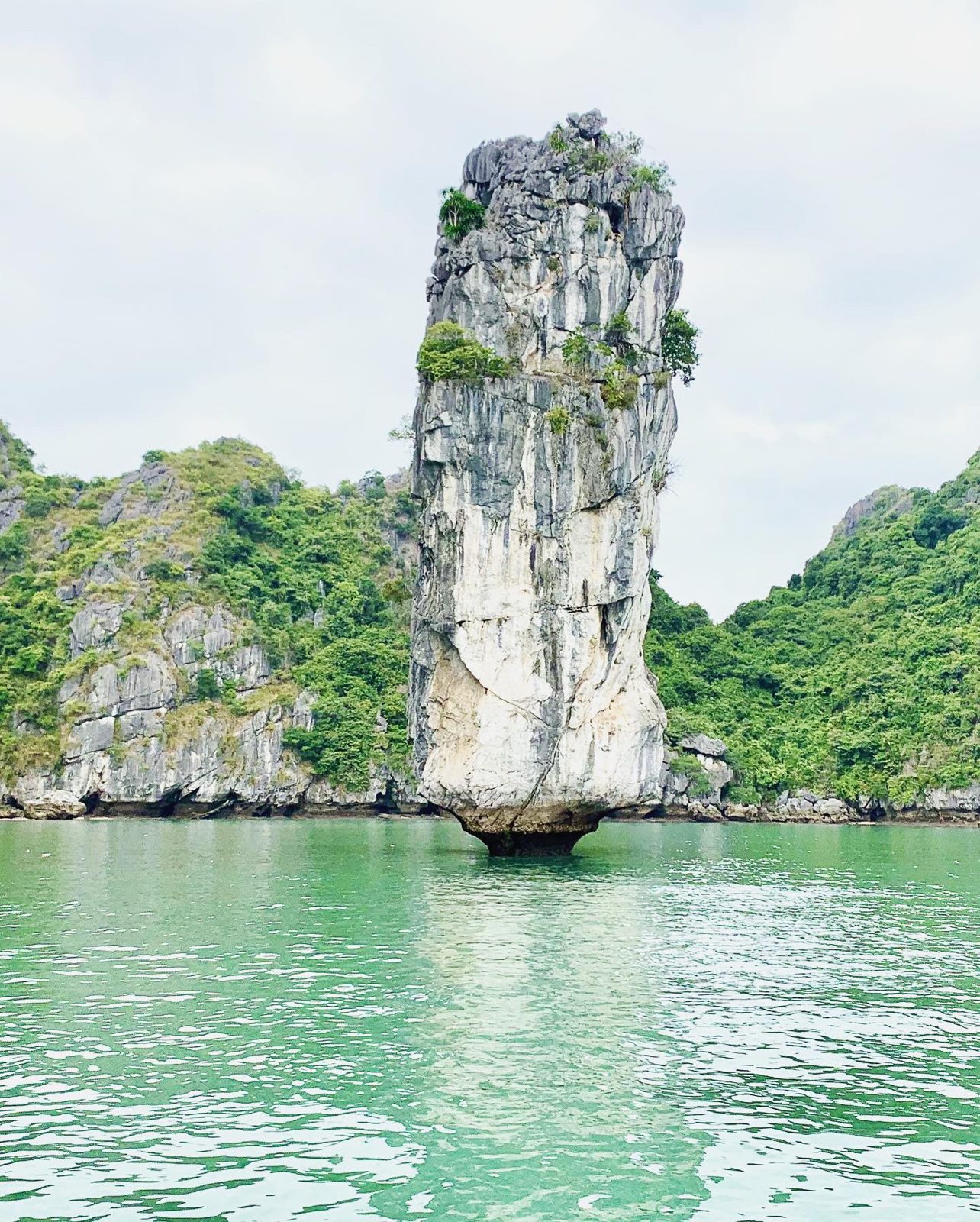 Tall limestone pinnacle island rising from green water in Lan Ha Bay